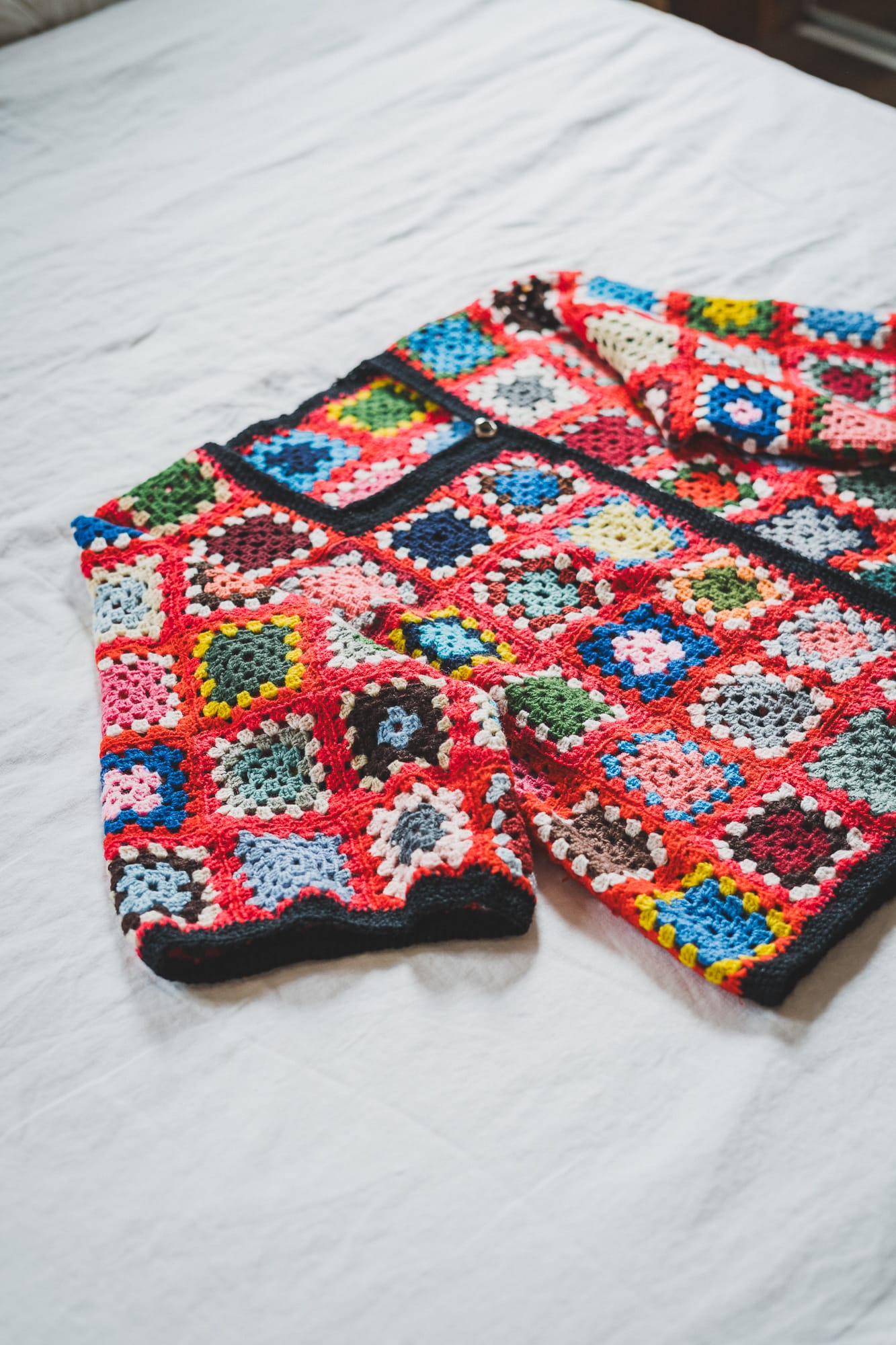 Flat Lay of Crochet Cardigan on White Bed Sheets