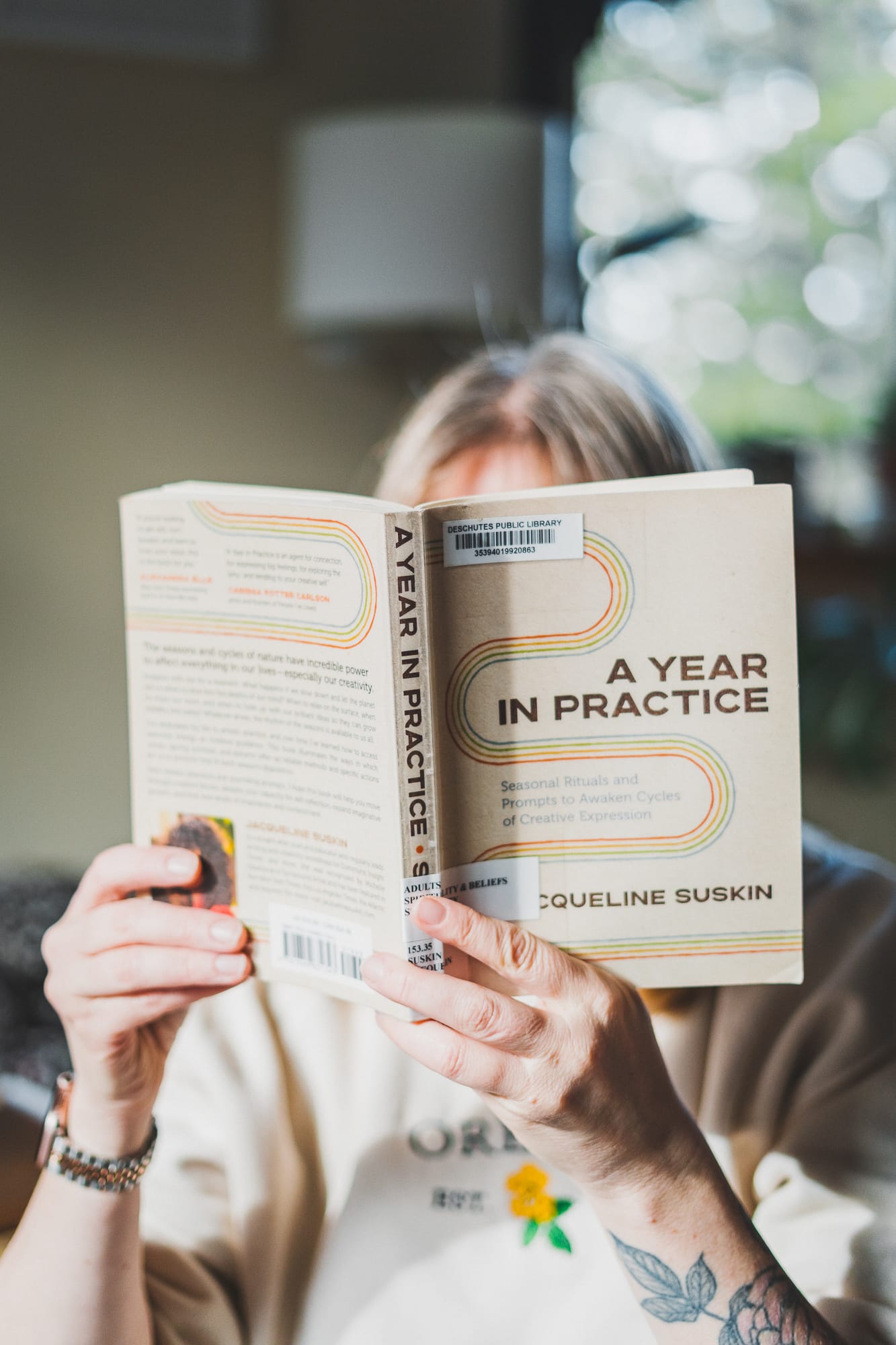 A person reads A Year in Practice by Jacqueline Suskin while sitting indoors, holding the book open so the cover and spine are clearly visible in soft natural light.