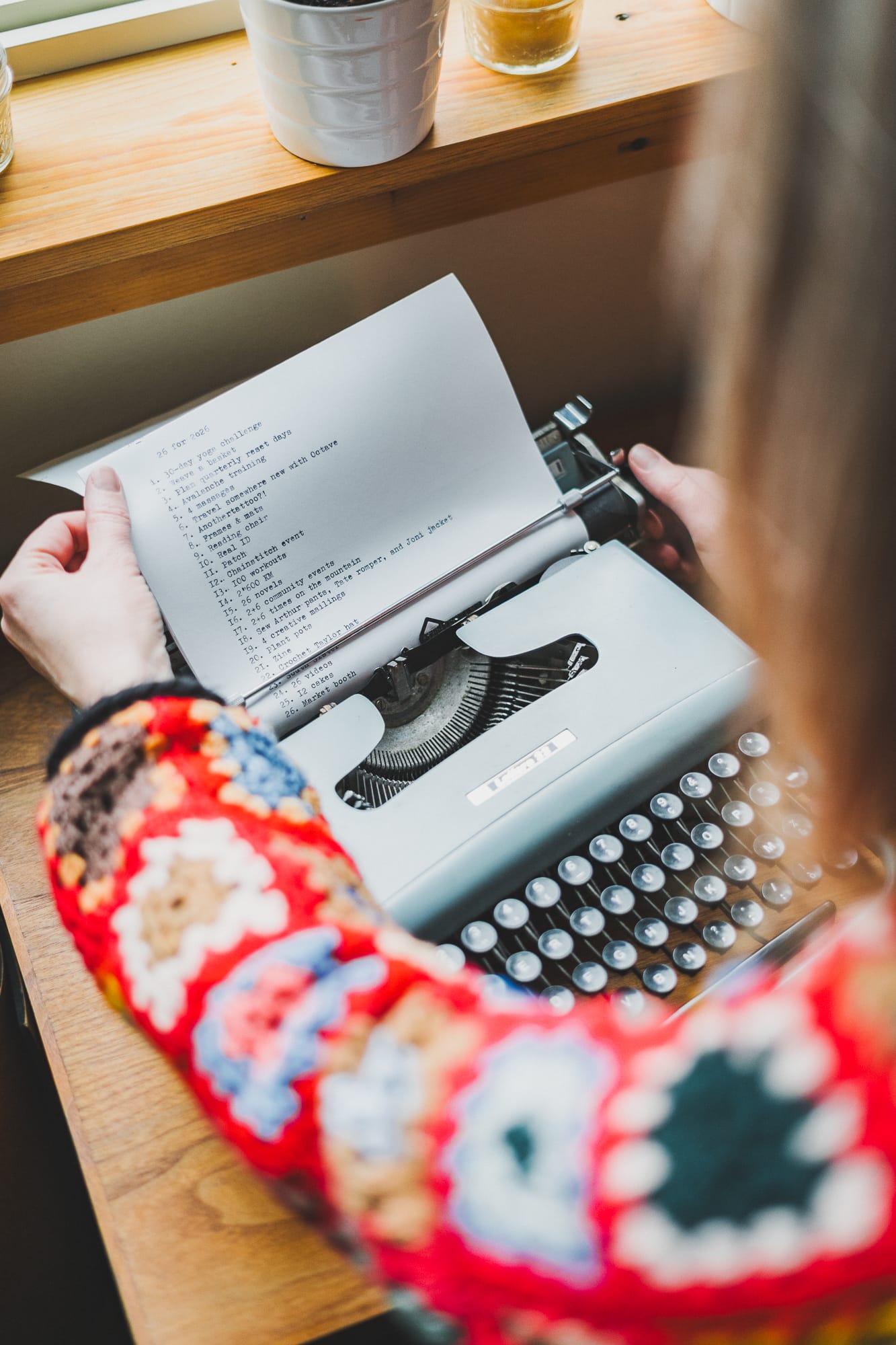 Close-up of hands holding a typewritten goals list in a vintage typewriter, sunlight coming through a window above.