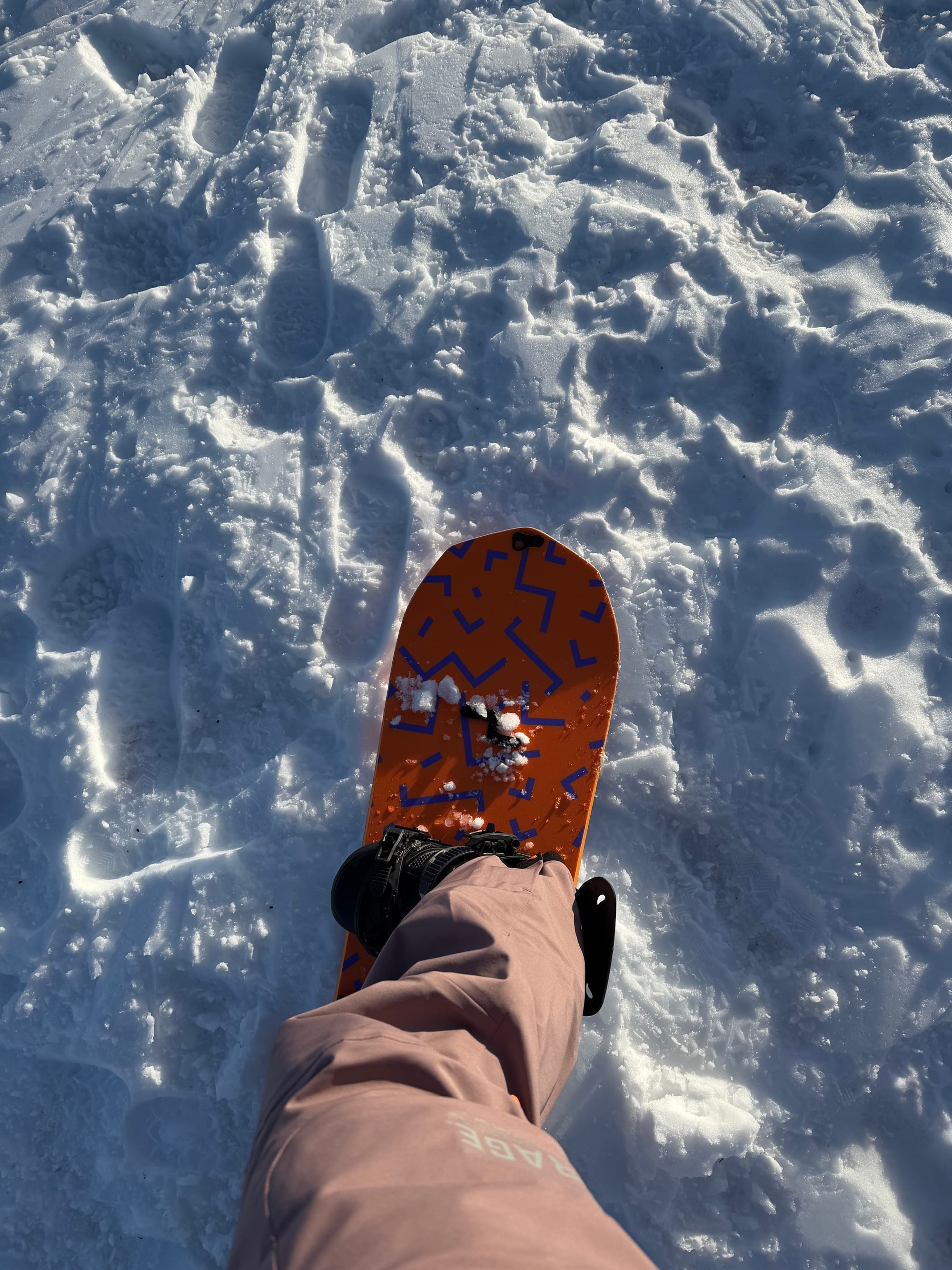Close-up of a splitboard in ride mode resting on textured snow, showing board graphics and fresh snow clumps.