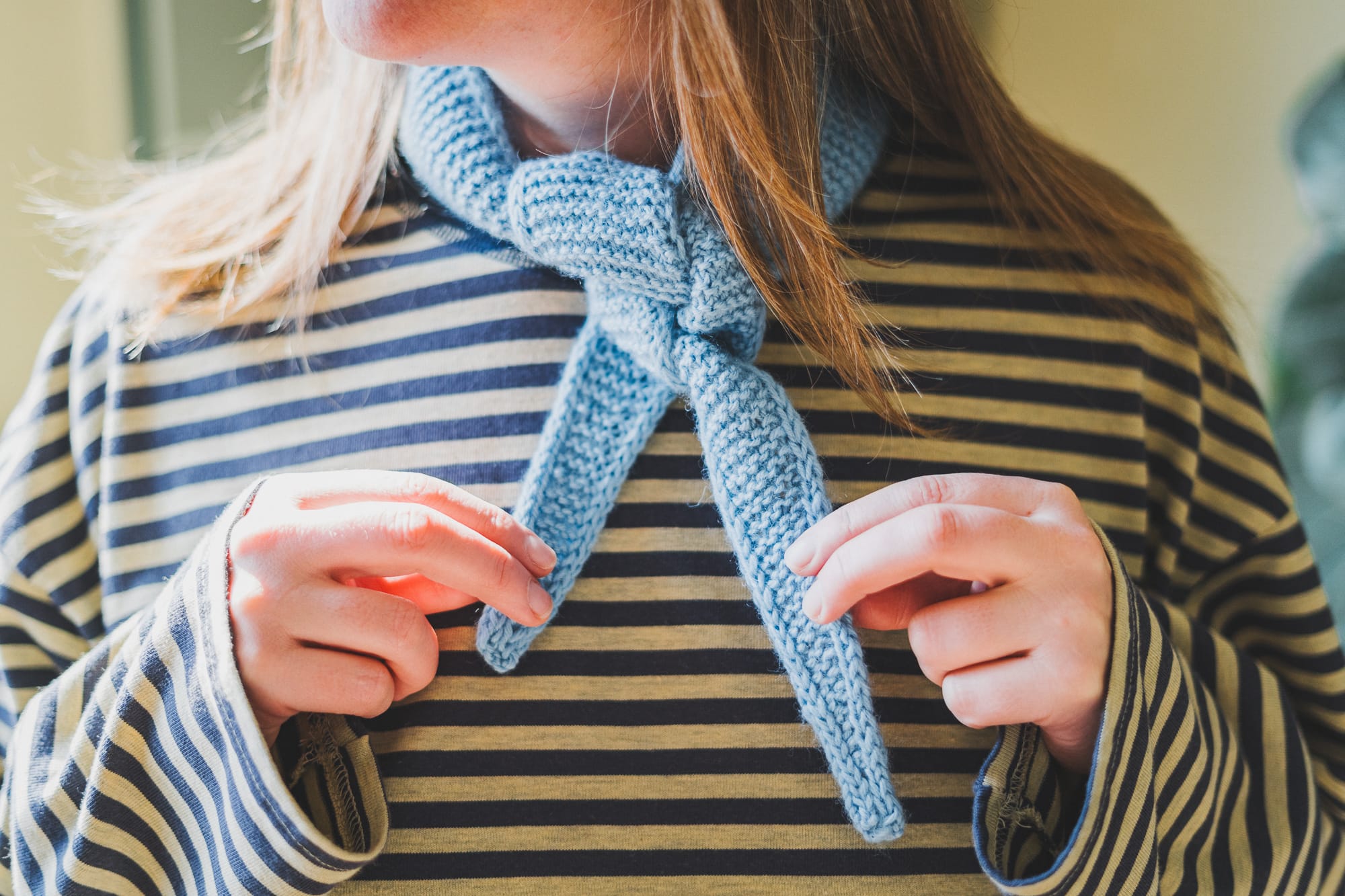 Close-up of the finished Sophie scarf by PetiteKnit tied at the neck, showing the garter stitch texture and triangular shape.